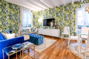 A living room with a blue sofa, a glass coffee table, a white TV stand, and patterned wallpaper.