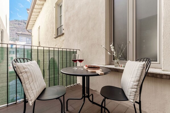 A balcony with two chairs, a small table, and a window with a view of a building and hills. - 05 Roma Visconti - My Home In Como (Como)