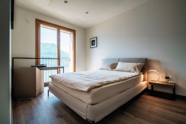 Ein Schlafzimmer mit Bett, Nachttisch mit Lampe, Fenster mit Bergblick und einem Balkon.
