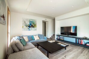 Ein modernes Wohnzimmer mit einem Ecksofa, einem Couchtisch, einem Fernseher und einem Bücherregal.