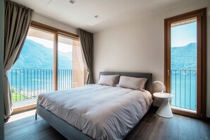 A bedroom with a bed, a bedside table, and a view of a lake and mountains.