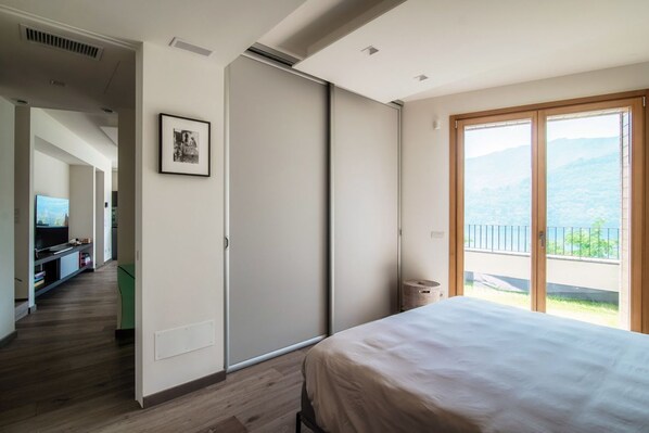 A bedroom with a bed, a sliding door, a framed picture, a small trash can, and a balcony with a view.