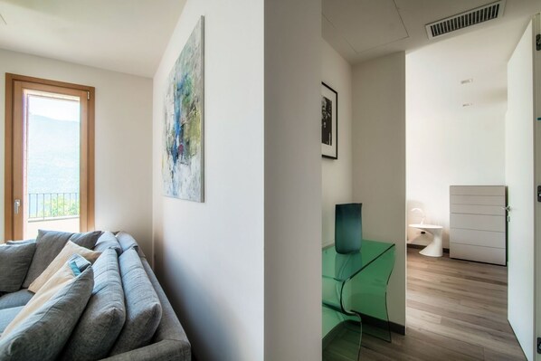 A modern living room with a sofa, a painting, and a view of the outdoors.
