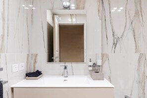 Een moderne badkamer met een wastafel van wit marmer, een spiegel en een handdoekrek.