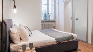 A bedroom with a bed, bedside table, lamp, window, radiator, and sliding door. - MG Home - MyHomeInComo (Como)