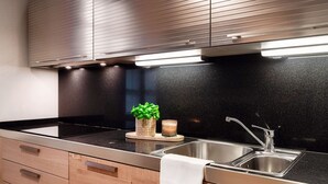 A modern kitchen with a black countertop, stainless steel sink, wooden cabinets, and a built-in range hood.