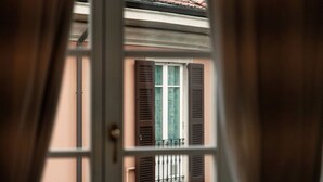 A view through a window with brown shutters, a balcony, and a building facade.