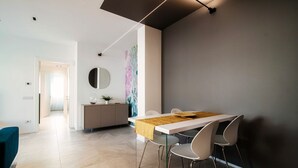 Un espace de salle à manger moderne avec une table blanche, quatre chaises, un vase central et un miroir fixé au mur.