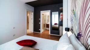 Une chambre à coucher avec un lit, un oreiller rouge, un oreiller blanc, un miroir et un mur orné d’un motif de feuilles.