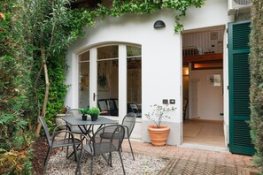 A patio with a table and chairs, a potted plant, and a view into the house. - The Artist's Nest - My Home In Como (Como)