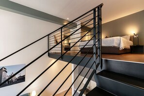 Een moderne trap met een metalen leuning die leidt naar een slaapkamer met een bed en nachtkastje.