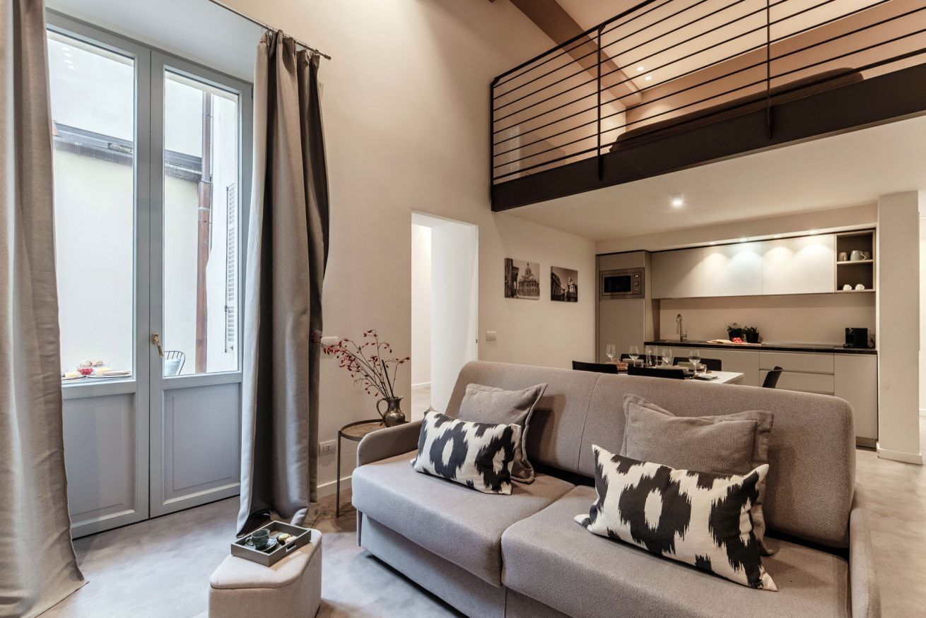 A modern living room with a grey sofa, a small side table, and a view of a kitchen.