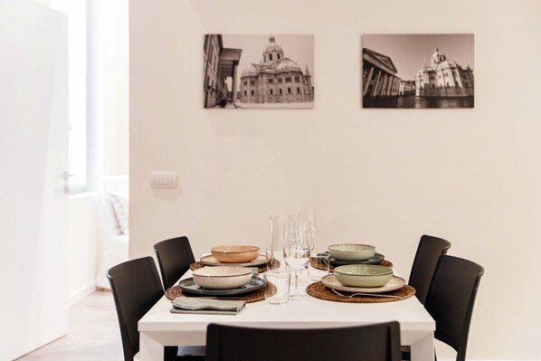 A dining table set with plates, glasses, and a pitcher, surrounded by chairs. - 04 Corte Visconti - MyHomeInComo (Como)