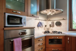 A modern kitchen with a microwave, oven, gas stove, and wooden cabinets. - My Sweet Garden - My Home In Como (Cassina Rizzardi)