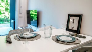 Une table à manger dressée avec des assiettes, des verres et un pichet, avec un tableau encadré et un téléviseur en arrière-plan.