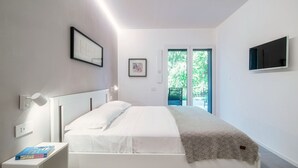 Une chambre moderne avec un lit, une table de chevet, un téléviseur fixé au mur et une fenêtre donnant sur un paysage verdoyant.