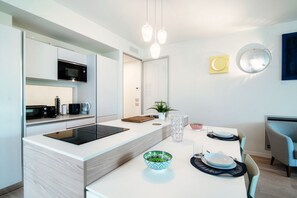 Una cocina moderna con una isla central, electrodomésticos integrados y un comedor con una mesa lista para dos personas.