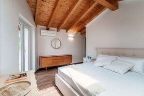 A bedroom with a wooden ceiling, a bed, a bedside table, a nightstand, a mirror, and a window.