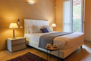 A bedroom with a bed, bedside tables, lamps, a small table with cups, and a view through a door. - Lakefront Contemporany - MyHomeInComo (Griante)