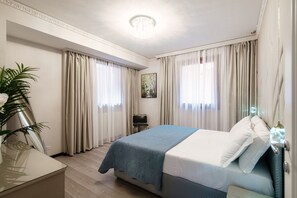 A hotel room with a bed, curtains, a plant, a painting, and a ceiling light. - Florissa - My Home In Como (Blevio)