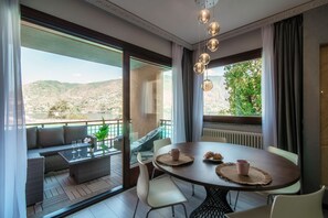 A modern room with a dining table, chairs, a sofa, and a view of a mountainous landscape. - Florissa - My Home In Como (Blevio)