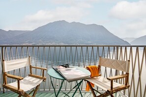 A balcony with two wooden chairs, a small table, and a view of a mountain and water. - La Casa del Pescatore - MyHomeInComo (Colonno)