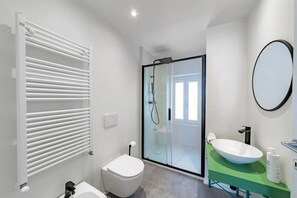 A modern bathroom with a glass shower enclosure, a white toilet, a green vanity with a white sink, and a round mirror. - La Casa del Pescatore - MyHomeInComo (Colonno)