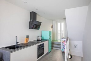 A modern kitchen with a built-in oven, a sink, a teal refrigerator, and a black range hood.