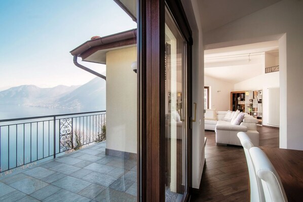 Un balcón con vistas a las montañas, un sofá blanco y un suelo de madera dentro de una habitación.