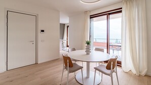 A modern room with a round dining table, four chairs, a ceiling light, a door, and a large window with curtains. - Bella Lì - MyHomeInComo (Menaggio)