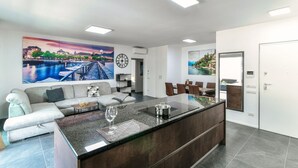 Eine moderne Küche mit einer zentralen Kochinsel, ein Essbereich mit einer Couch und Stühlen, sowie ein Wohnzimmer mit Couch und Couchtisch.