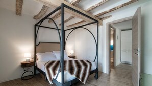 A four-poster bed with a wooden headboard, a bedside table with a lamp, and a striped throw blanket. - Acqua - My Home in Como (Moltrasio)
