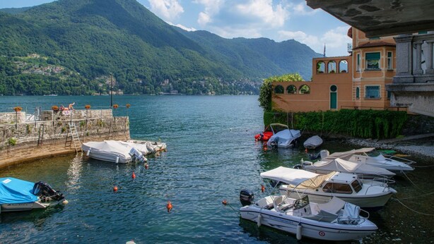 A lake with boats docked, a mountain in the background, and a building with arched windows. - Acqua - My Home in Como (Moltrasio)