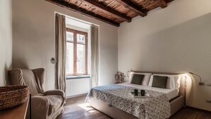 A bedroom with a bed, a chair, a window, and wooden beams on the ceiling.