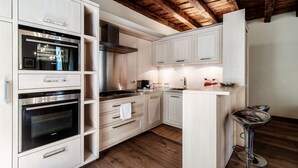 A modern kitchen with built-in ovens, a stainless steel range hood, and a bar stool.