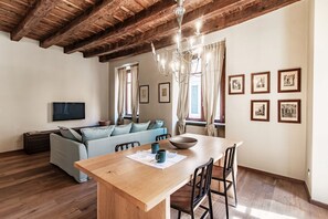 Ein gemütlicher Wohnbereich mit Holzboden, einem Esstisch mit Stühlen, einer Couch, einem Fernseher und gerahmten Bildern an der Wand.