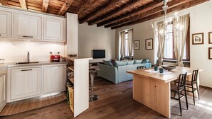 A modern kitchen with wooden beams, a dining area with a wooden island, and a living room with a sofa and curtains.