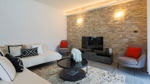 A modern living room with a stone wall, a sofa, two armchairs, a coffee table, and a flat-screen TV.