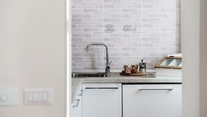 A kitchen with a tiled backsplash, a stainless steel sink, and a countertop with a bread basket.