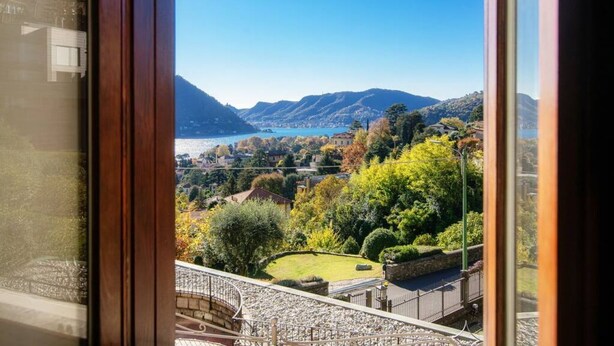 A view from a window overlooking a lake, mountains, and a well-maintained garden.