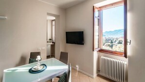 A dining area with a glass table, chairs, a TV, and a window with a view.