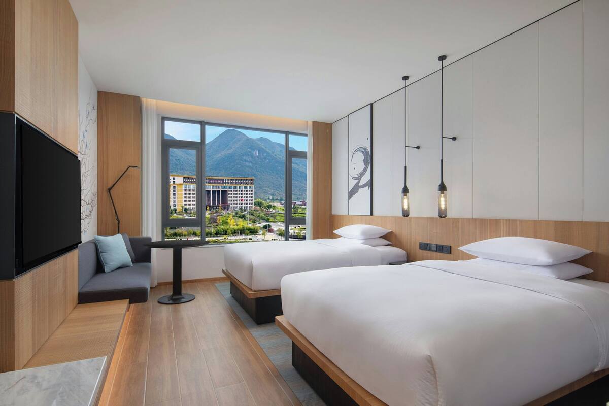 Une chambre d’hôtel moderne avec deux lits, une télévision et une grande fenêtre donnant sur les montagnes.