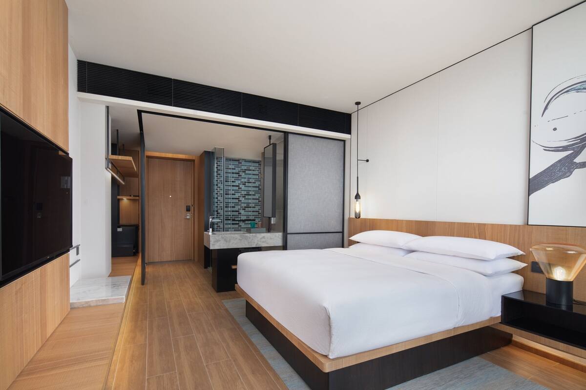 Une chambre d’hôtel moderne avec un grand lit, une télévision, une salle de bain avec un miroir et une vue sur le couloir.