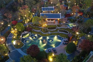 Vue aérienne d’un bâtiment de style japonais traditionnel, entouré de jardins aménagés, comprenant un bassin à carpes koï et des espaces de détente.