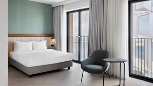 A hotel room with a bed, a chair, a small table, and a large window with curtains. - Fairfield By Marriott Copenhagen Nordhavn (Copenhagen)