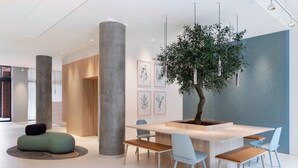 A modern dining area with a large table, chairs, and a central tree planter. - Fairfield By Marriott Copenhagen Nordhavn (Copenhagen)