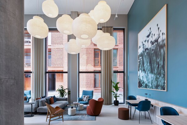 A modern interior with a large window, a sofa, a blue chair, and a table. - Fairfield By Marriott Copenhagen Nordhavn (Copenhagen)