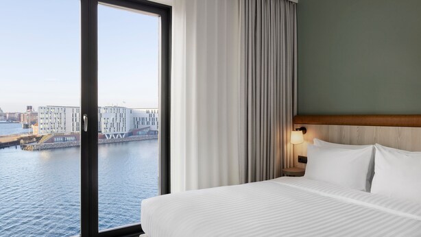A hotel room with a large window offering a view of a cityscape and water. - Fairfield By Marriott Copenhagen Nordhavn (Copenhagen)