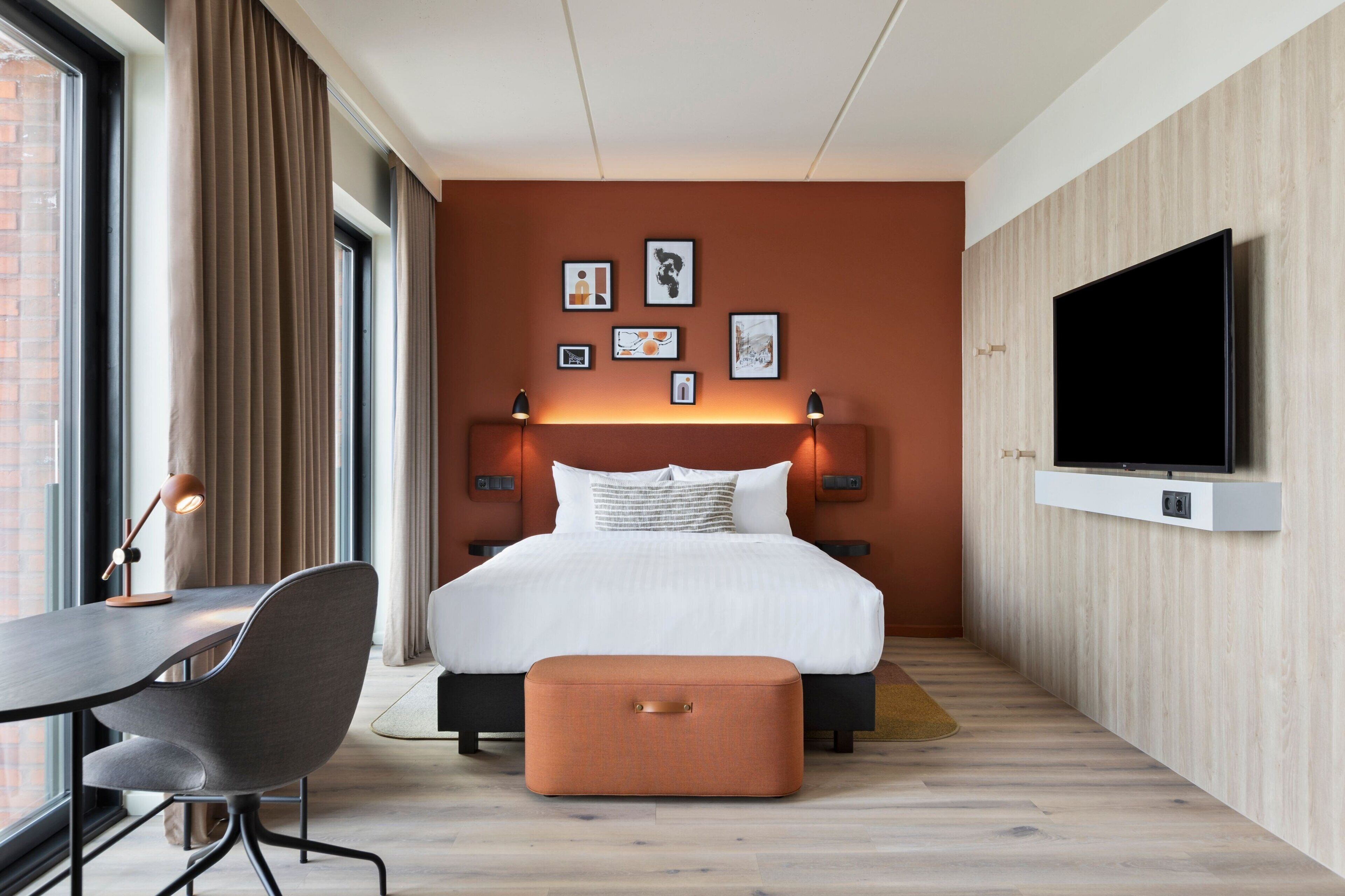 Una habitación de hotel moderna con una cama grande, un escritorio, una silla, un televisor y obras de arte en la pared.