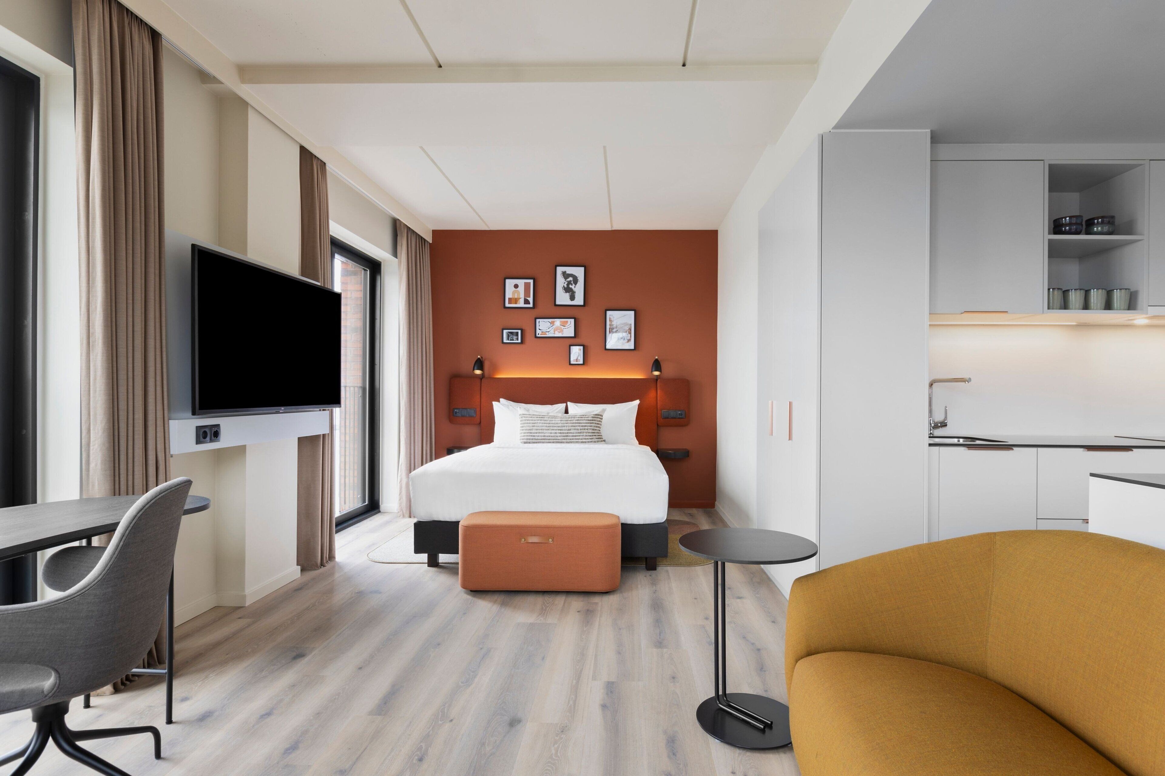 A hotel room with a bed, a desk, a chair, a television, and a kitchenette.